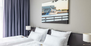 Modernes Hotelzimmer mit zwei Einzelbetten, blauen Vorhängen und maritimem Wandbild.