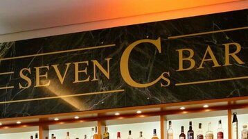 Elegante Hotelbar mit beleuchteten Regalen voller Spirituosen, Ledersesseln und großen Fenstern mit Vorhängen.