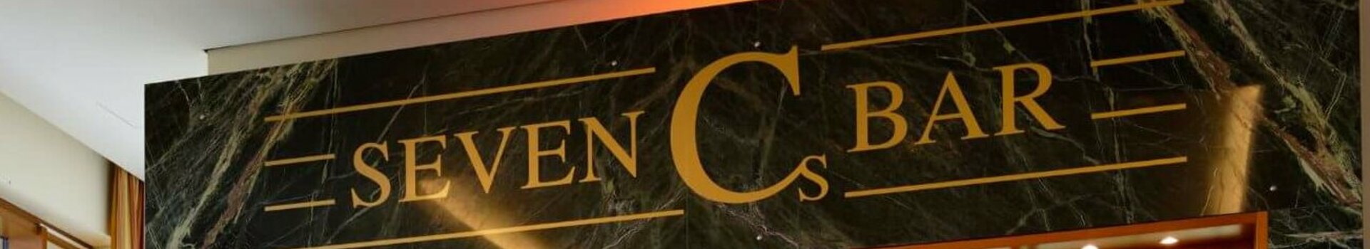 Elegante Hotelbar mit beleuchteten Regalen voller Spirituosen, Ledersesseln und großen Fenstern mit Vorhängen.