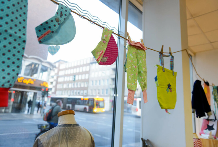 ATLANTIC Hotel Sail City | Upcycling-Offensive "GRÜNER FADEN" Ein Schaufenster mit bunter Kinderkleidung an einer Leine, im Hintergrund eine Straßenszene.