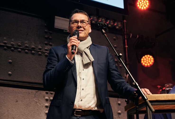 A man in a suit speaks into a microphone on a stage in the ATLANTIC Hotel Sail City.