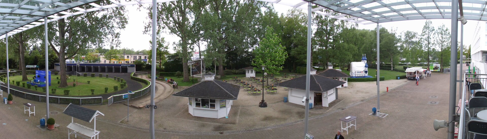 Grüner Innenhof mit Bäumen und kleinen Pavillons, umgeben von Gehwegen am ATLANTIC Hotel Galopprennbahn Bremen.
