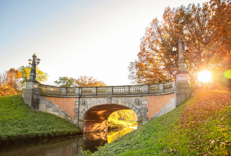 Stone bridge in autumn light, surrounded by colorful foliage and green grass, with a stream below.
