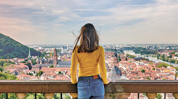 Eine Frau steht an einem Aussichtspunkt mit Blick über Heidelberg