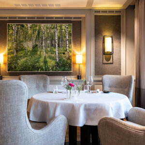Elegantes Restaurant mit gedecktem Tisch, bequemen Sesseln und einem Gemälde von Birkenwald an der Wand.