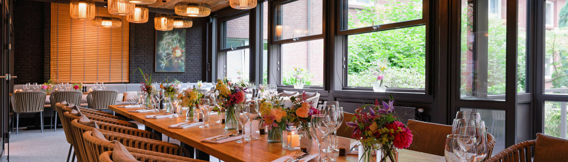 Veranstaltungsraum Wintergarten im ATLANTIC Hotel Landgut Horn Eleganter Speisesaal mit gedecktem Holztisch, Blumenarrangements und modernen Lampen im ATLANTIC Hotel Landgut Horn Bremen.