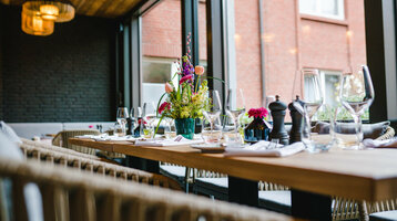 Windergarten at the ATLANTIC Hotel Landgut Horn Bremen Elegant, laid table in the restaurant with flower arrangement and view through large windows in the ATLANTIC Hotel Landgut Horn.