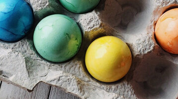 Bunte Ostereier in einem Eierkarton auf Holzuntergrund.