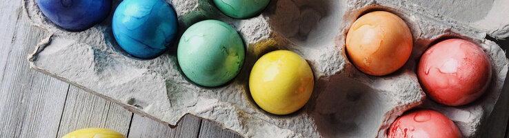 Bunte Ostereier in einem Eierkarton auf Holzuntergrund.