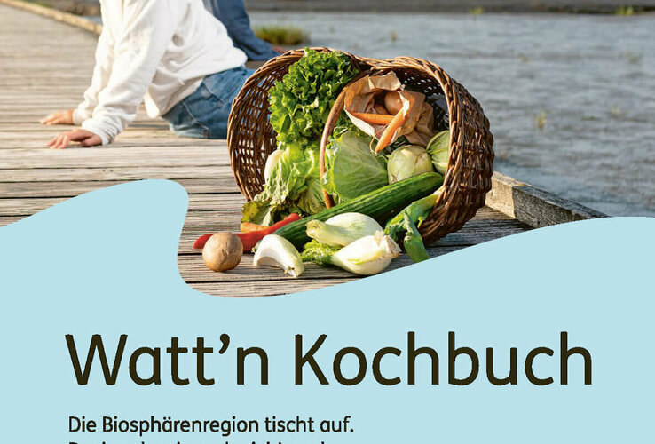 Ein Paar sitzt auf einem Steg am Wasser, daneben ein Korb mit frischem Gemüse.