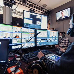 Techniker steuern ein virtuelles Event mit mehreren Bildschirmen und Computern in einem Kontrollraum.
