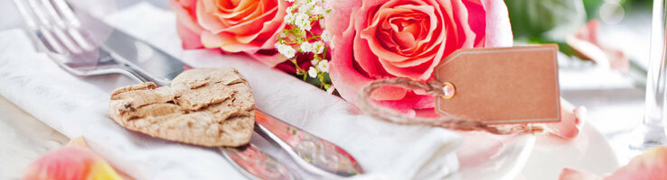 ATLANTIC Grand Hotel Travemünde Elegante Tischdekoration mit rosa Rosen, Besteck auf Serviette und Herzanhänger im ATLANTIC Grand Hotel Travemünde.