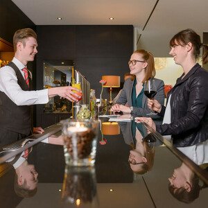 Bartender serves cocktails to two women at the stylish hotel bar of the ATLANTIC Hotel Lübeck.