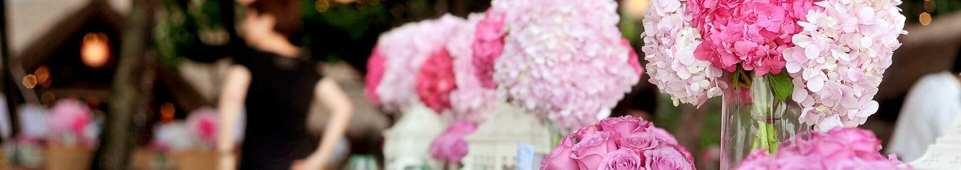 Elegant, festively decorated outdoor table with pink flower arrangements and atmospheric lighting.