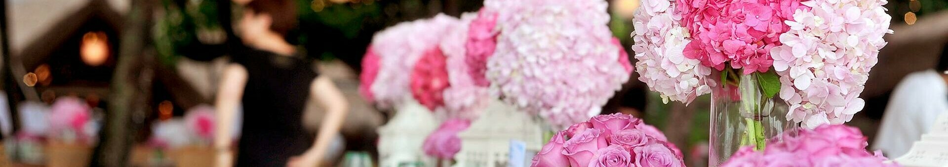 Elegante, festlich gedeckte Tafel im Freien mit rosa Blumenarrangements und stimmungsvoller Beleuchtung.