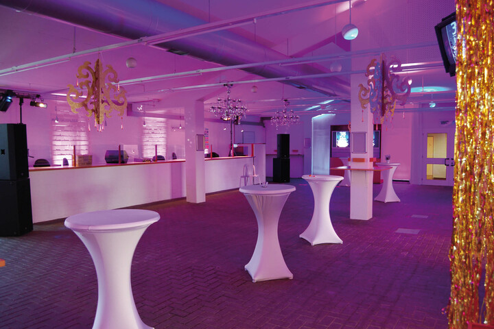 Unsere Wetthalle als Eventlocation  Moderner Veranstaltungsraum mit Stehtischen, lila Beleuchtung und dekorativen Kronleuchtern im ATLANTIC Hotel Galopprennbahn.