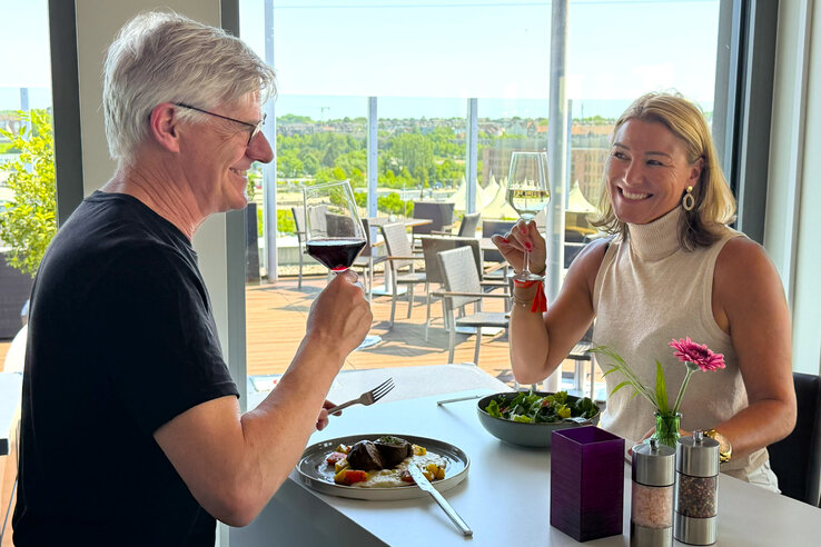 Zwei Menschen stoßen beim Essen mit Wein an.