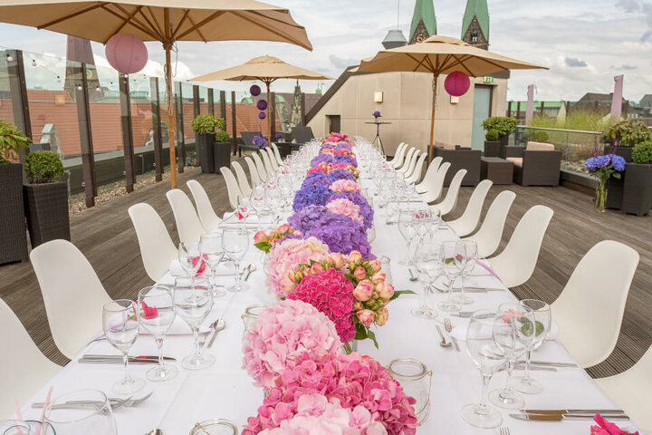 Hochzeitstafel auf der Dachterrase des ATLANTIC Grand Hotel Bremen Lange Tafel mit weißen Stühlen und bunten Blumenarrangements auf einer Dachterrasse des ATLANTIC Grand Hotel Bremen.