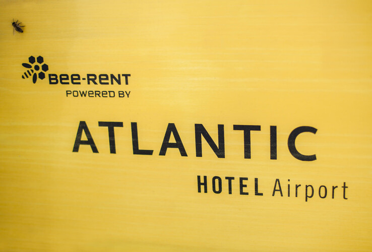 Gelbes Schild mit "Bee-Rent powered by ATLANTIC Hotel Airport" und einer Biene links oben.