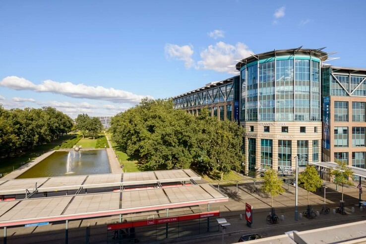 ATLANTIC Hotel Airport Bremen, modernes Gebäude mit Glasfassade, Park und Teich im Vordergrund, bei sonnigem Wetter.