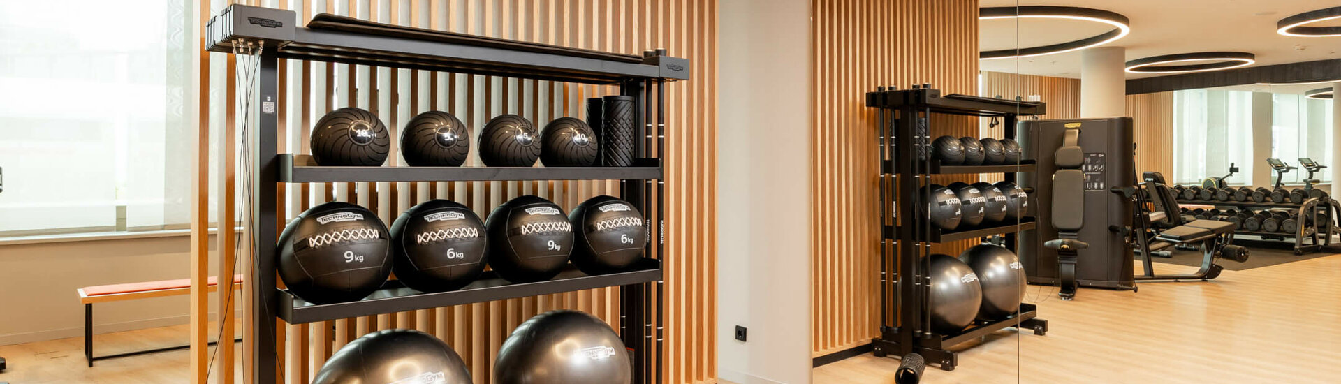 Moderner Fitnessraum im ATLANTIC Hotel Heidelberg mit Medizinbällen, Spiegelwand und Trainingsgeräten.