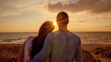 Paar genießt Sonnenuntergang am Strand mit Blick auf die Ostsee, warmes Licht und ruhige Atmosphäre.