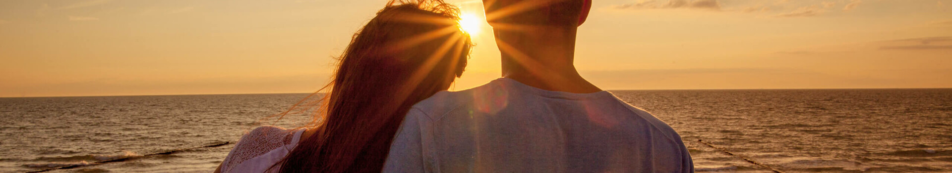 Arrangement Zeit zu Zweit in Travemünde Paar genießt Sonnenuntergang am Strand mit Blick auf die Ostsee, warmes Licht und ruhige Atmosphäre.