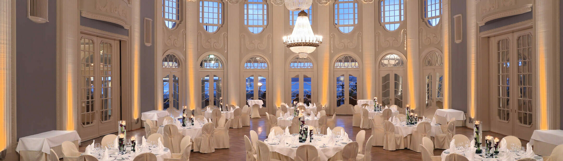 ATLANTIC Grand Hotel Travemünde - Ballsaal Eleganter Ballsaal im ATLANTIC Grand Hotel Travemünde mit Kronleuchter, runden Tischen und weißen Stühlen.