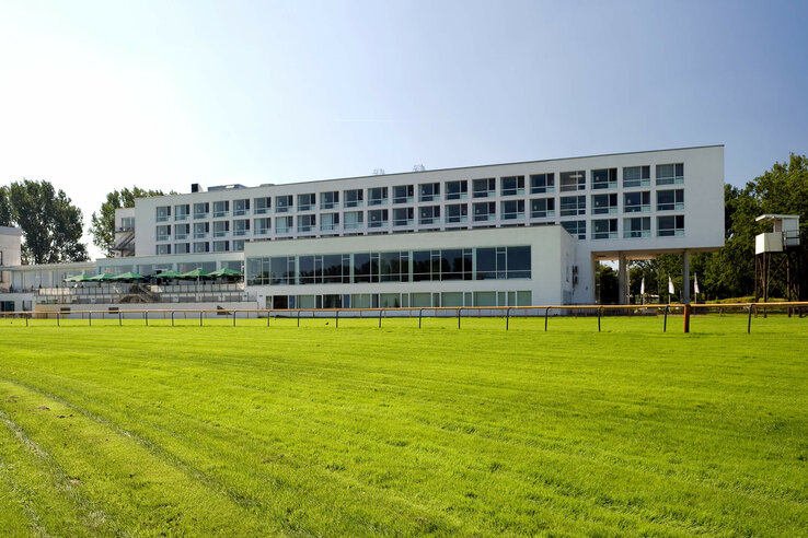 ATLANTIC Hotel Galopprennbahn: Modernes Gebäude mit großen Fenstern, umgeben von grüner Rasenfläche.