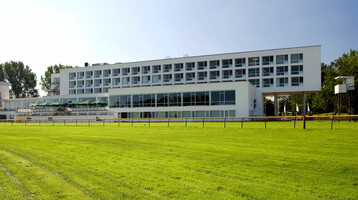 ATLANTIC Hotel Galopprennbahn: Modernes Gebäude mit großen Fenstern, umgeben von grüner Rasenfläche.