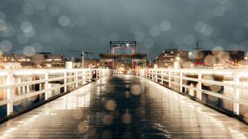A walk on the Horn Bridge in the evening Night shot of an illuminated footbridge with blurred lights and buildings in the background.