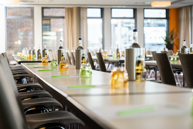 Konferenzraum im ATLANTIC Hotel Kiel mit gedeckten Tischen, Getränken und Stühlen, helle Fenster im Hintergrund.