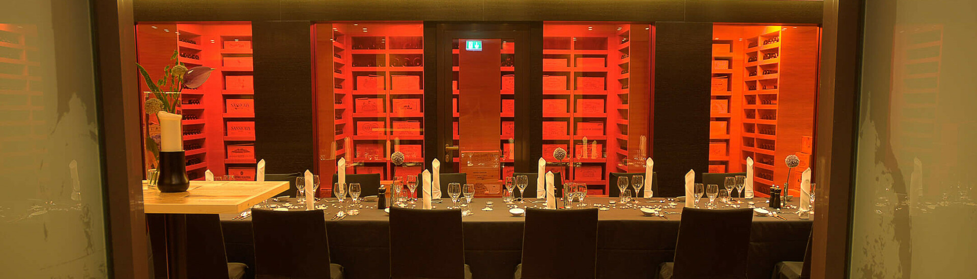 Weintresor im ATLANTIC Hotel Kiel Elegantes Restaurant im ATLANTIC Hotel Kiel mit langer, festlich gedeckter Tafel und beleuchtetem Weinregal.