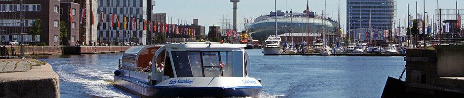 Blick auf das ATLANTIC Hotel Sail City in Bremerhaven, mit Boot auf dem Wasser und moderner Architektur im Hintergrund.