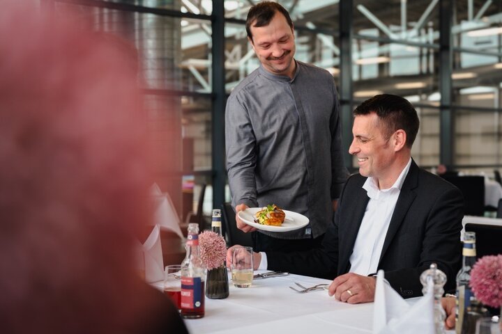 Gäste im Restaurant Gottlieb Bremen Ein Kellner serviert einem lächelnden Gast in einem eleganten Restaurant ein Gericht.