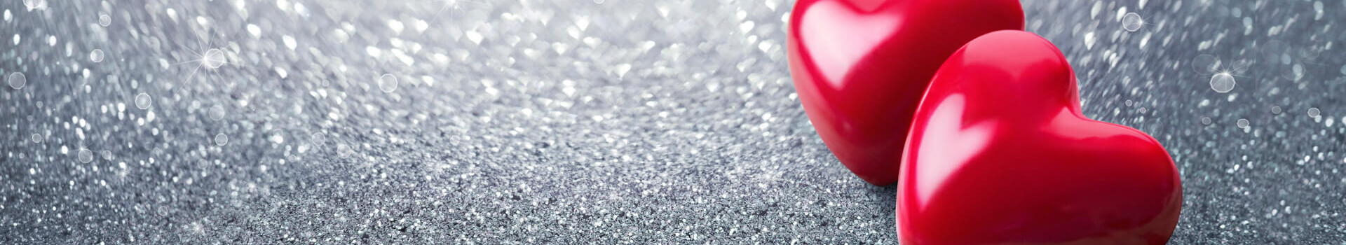 Valentinstag-Party im ATLANTIC Hotel Münster Zwei rote Herzen auf glitzerndem, silbernen Hintergrund.