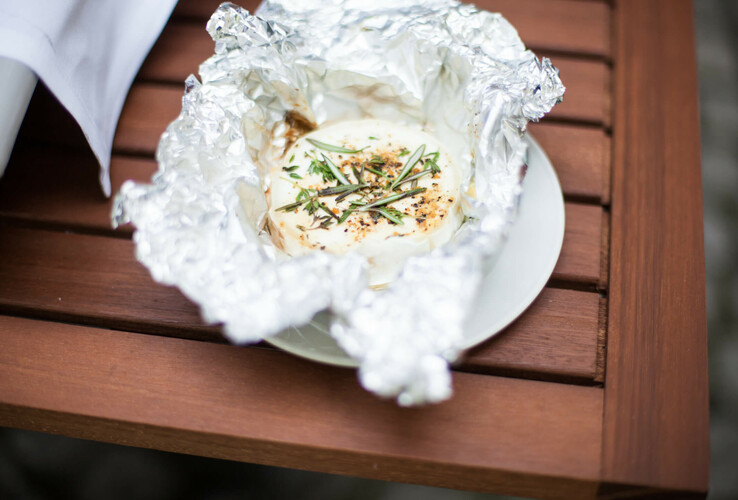 Baked cheese with herbs in aluminum foil on a wooden table at the ATLANTIC Hotel Airport Bremen.