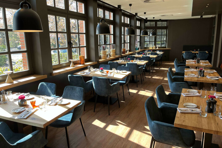 Restaurant VICTORIAN im ATLANTIC Hotel Landgut Horn Bremen Helles Restaurant mit Holztischen, blauen Stühlen und großen Fenstern im ATLANTIC Hotel Landgut Horn Bremen.