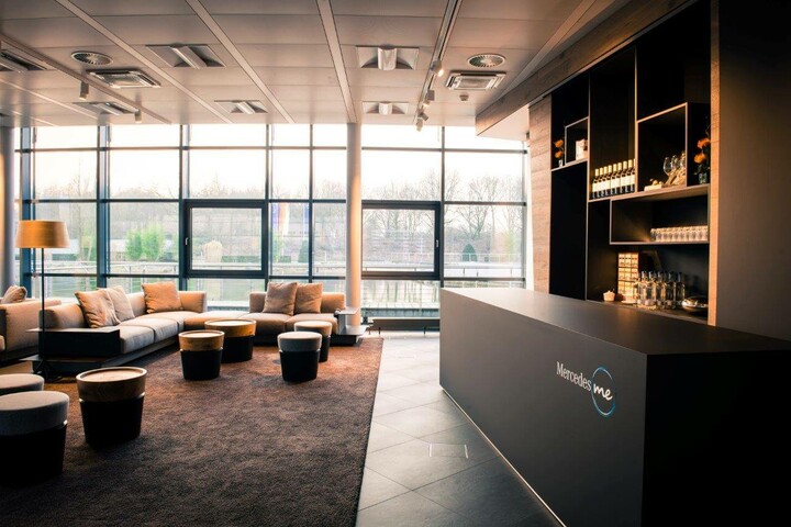 Moderne Hotel-Lounge mit großen Fenstern, gemütlichen Sofas, Hockern und einem Tresen mit Regalen im Hintergrund.