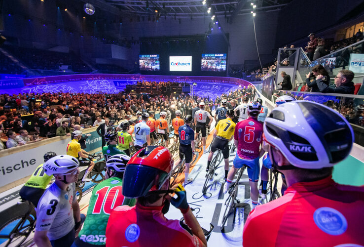 Bild der Fahrradfahrer bei den Sixdays vor dem Start auf der Fahrbahn, voller bunter Trikots und Helme