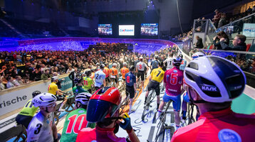Bild der Fahrradfahrer bei den Sixdays vor dem Start auf der Fahrbahn, voller bunter Trikots und Helme