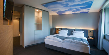 Modernes Hotelzimmer mit Doppelbett, stilvollen Möbeln, großem TV und Decke mit Himmelmotiv im ATLANTIC Hotel Airport Bremen.