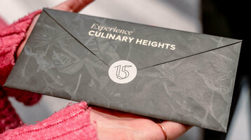 Hände halten einen eleganten Umschlag mit der Aufschrift "Experience Culinary Heights" im ATLANTIC Hotel Heidelberg.