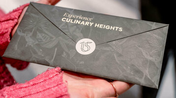 Hands holding an elegant envelope labeled "Experience Culinary Heights" at the ATLANTIC Hotel Heidelberg.