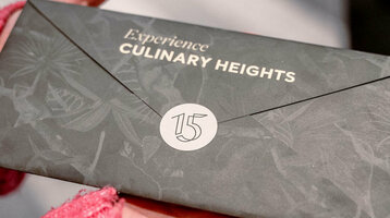 Hände halten einen eleganten Umschlag mit der Aufschrift "Experience Culinary Heights" im ATLANTIC Hotel Heidelberg.