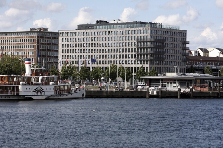 Blick auf das ATLANTIC Hotel Kiel von der Förde aus, mit einem Schiff im Vordergrund und blauem Himmel.