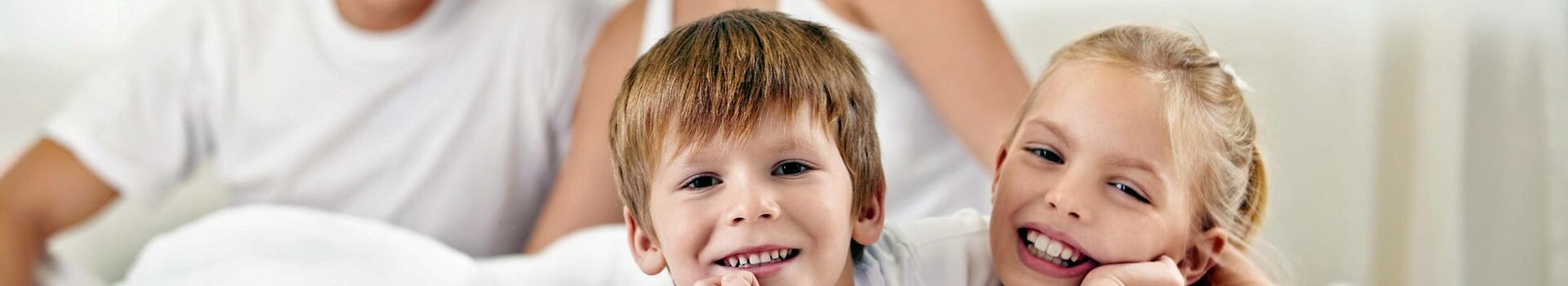 Familie entspannt lächelnd auf einem Bett im ATLANTIC Hotel Lübeck, helle und freundliche Atmosphäre.