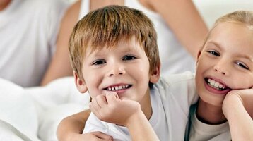 Familie entspannt lächelnd auf einem Bett im ATLANTIC Hotel Lübeck, helle und freundliche Atmosphäre.