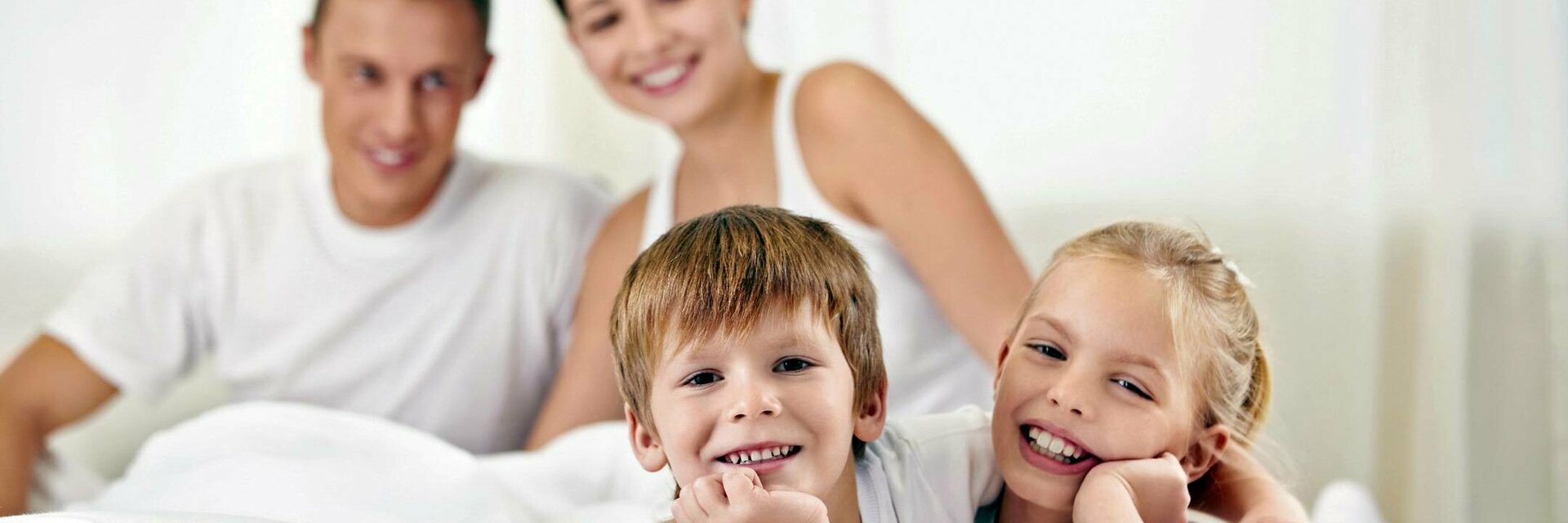 Familie entspannt lächelnd auf einem Bett im ATLANTIC Hotel Lübeck, helle und freundliche Atmosphäre.