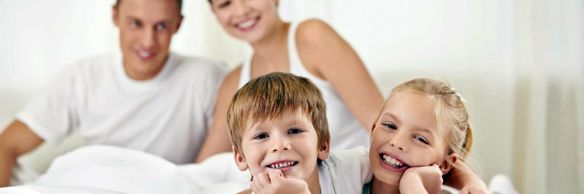 Family relaxing with a smile on a bed in the ATLANTIC Hotel Lübeck, bright and friendly atmosphere.
